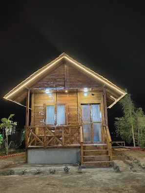 A wooden cabin with a pitched roof, large windows, and a porch with steps leading to the entrance.