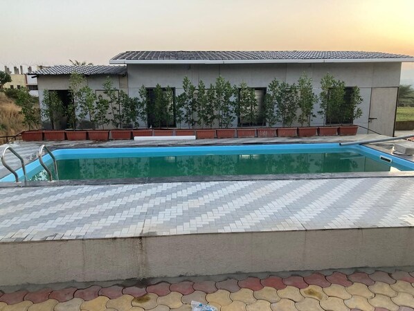 A swimming pool with a tiled deck, surrounded by potted plants and a building with a tiled roof.