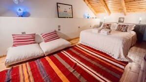 Une chambre confortable avec un lit, un canapé, un tapis rayé aux couleurs vives et un plafond avec des poutres en bois.