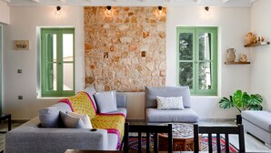 Un salon chaleureux avec un mur en pierre, deux fenêtres vertes et une table basse en bois.