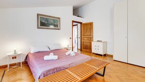 A bedroom with a bed, bedside tables, a bench, a wardrobe, and a door leading to another room. - Colosseum Terrace Penthouse (Rome)