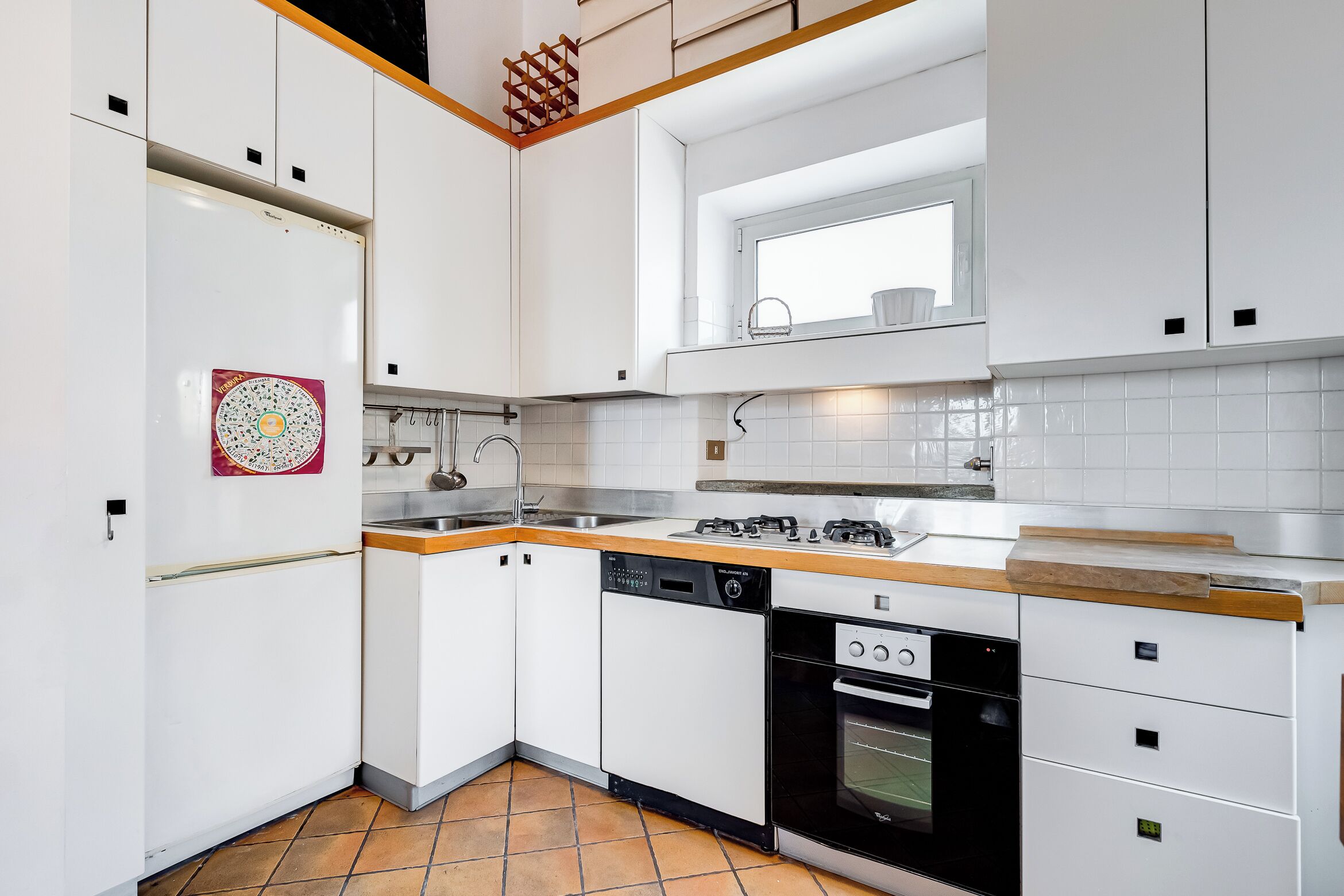 A modern kitchen with white cabinets, a dishwasher, an oven, and a wooden countertop.