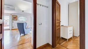 A modern interior with a wooden floor, a blue armchair, a white cabinet, and a door leading to another room. - Colosseum Terrace Penthouse (Rome)