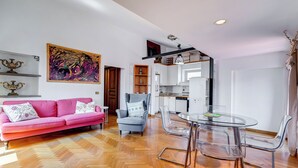 A modern living room with a pink sofa, a grey armchair, and a glass dining table with chairs. - Colosseum Terrace Penthouse (Rome)