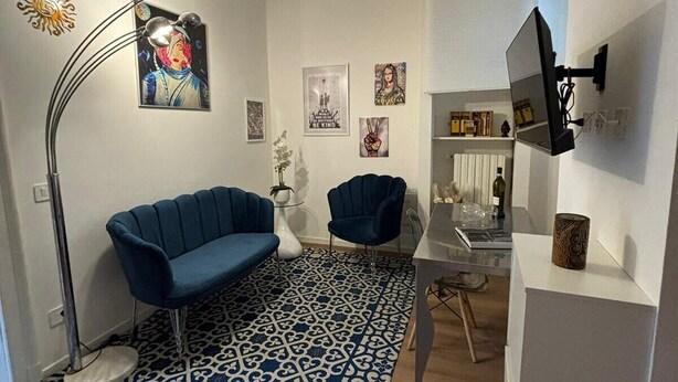 Een moderne woonkamer met een blauw gestreept tapijt, een blauwe bank, een vloerlamp en een aan de muur bevestigde televisie.
