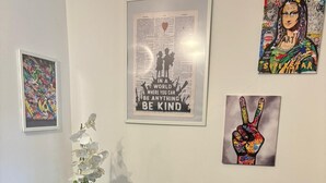 Een woonkamer met twee blauwe fauteuils, een glazen salontafel met een witte orchidee en drie ingelijste kunstwerken aan de muur.
