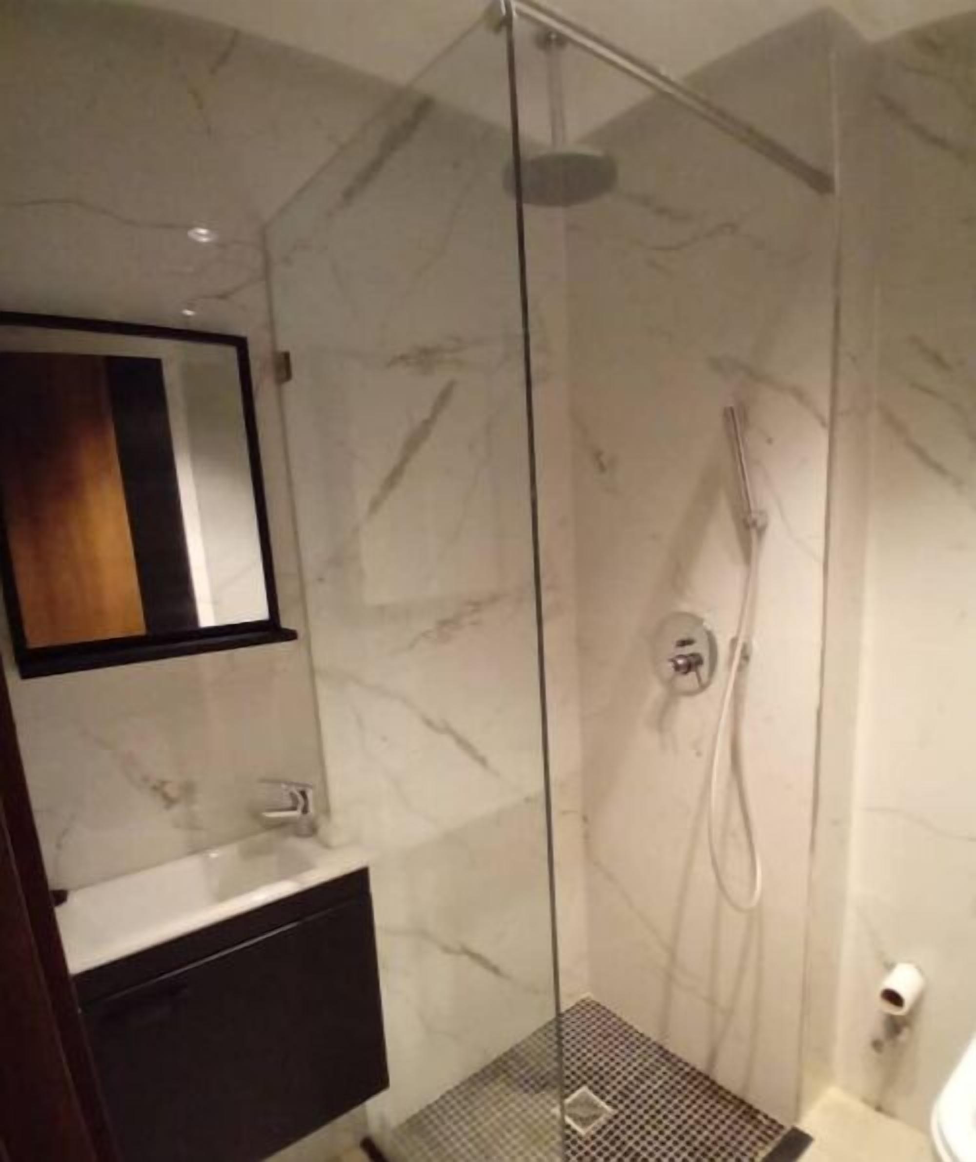 Une salle de bain moderne avec une douche à parois de verre, un mur en marbre et un meuble-lavabo en bois.