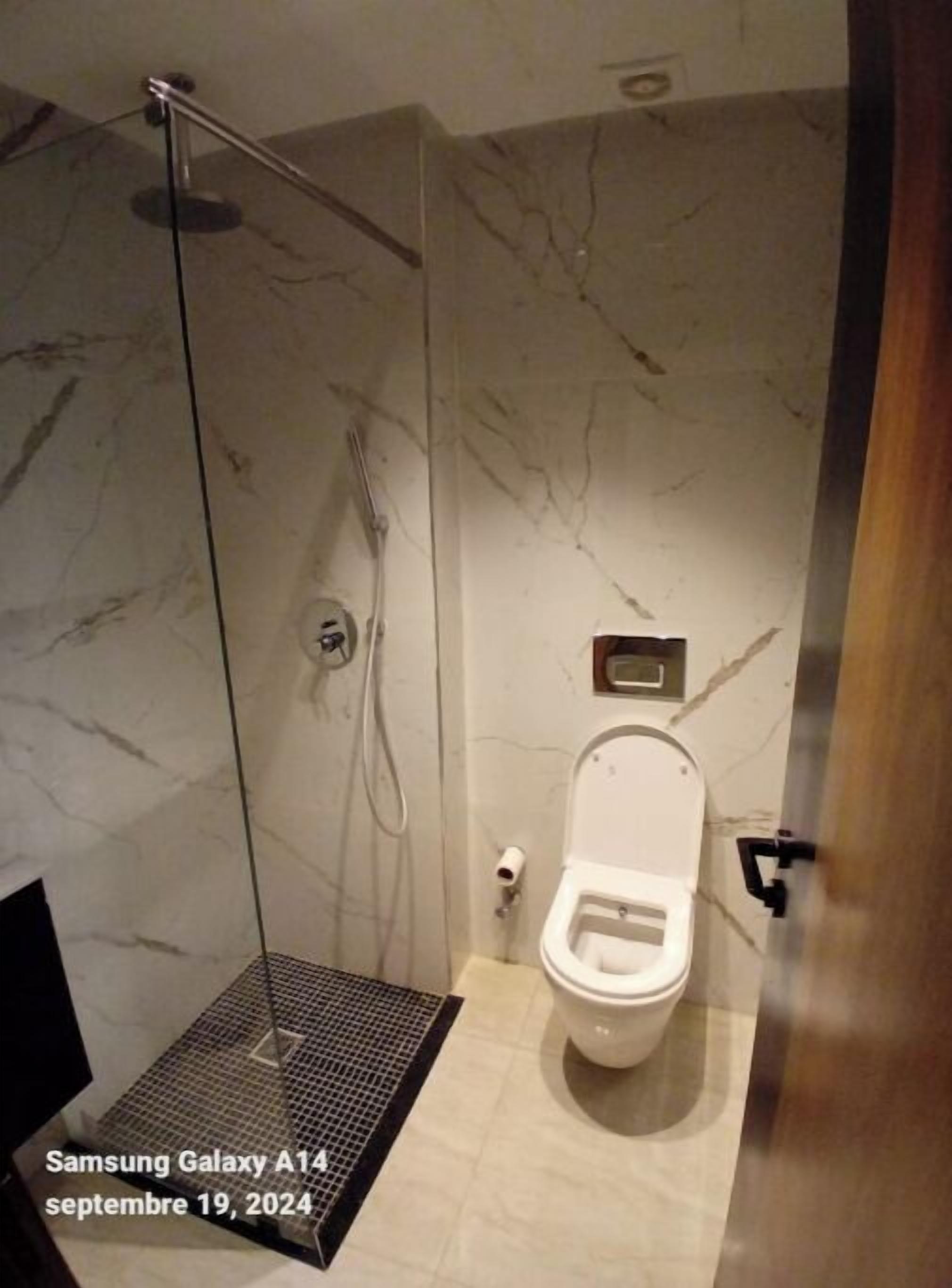 Un baño moderno con ducha, inodoro y un lavamanos pequeño.