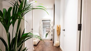 A hallway with a wooden floor, white walls, and a large potted plant. - Luxurious Haven in Battersea  (London)