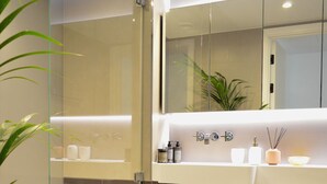 A modern bathroom with a glass shower enclosure, a bathtub, a toilet, and a vanity with a mirror. - Luxurious Haven in Battersea  (London)