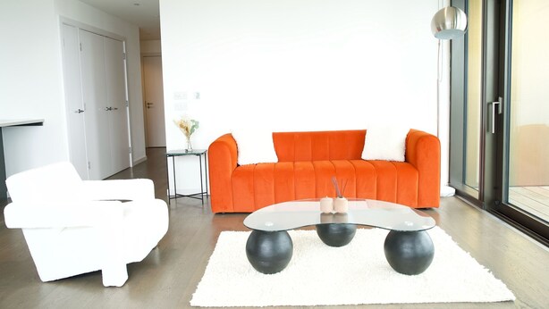 A modern living room with a white sofa, an orange sofa, and a glass coffee table. - Luxurious Haven in Battersea  (London)