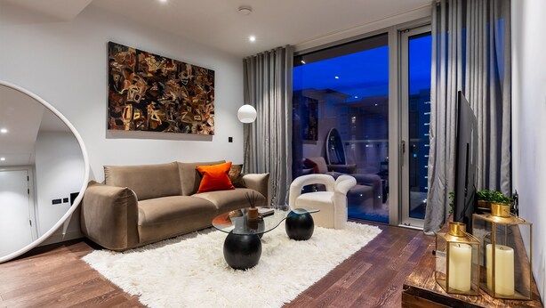 A modern living room with a brown sofa, a glass coffee table, and a white shag rug. - Luxurious Haven in Battersea  (London)