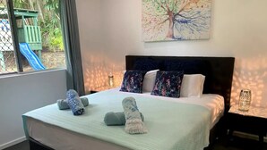 Een net opgemaakt bed met een lichtgroene dekbedovertrek, twee opgerolde handdoeken, een donker hoofdbord en kussens met een bloemenprint.