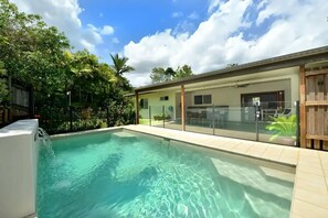 Una piscina amb aigua cristal·lina, envoltada per una tanca i vegetació exuberanta.