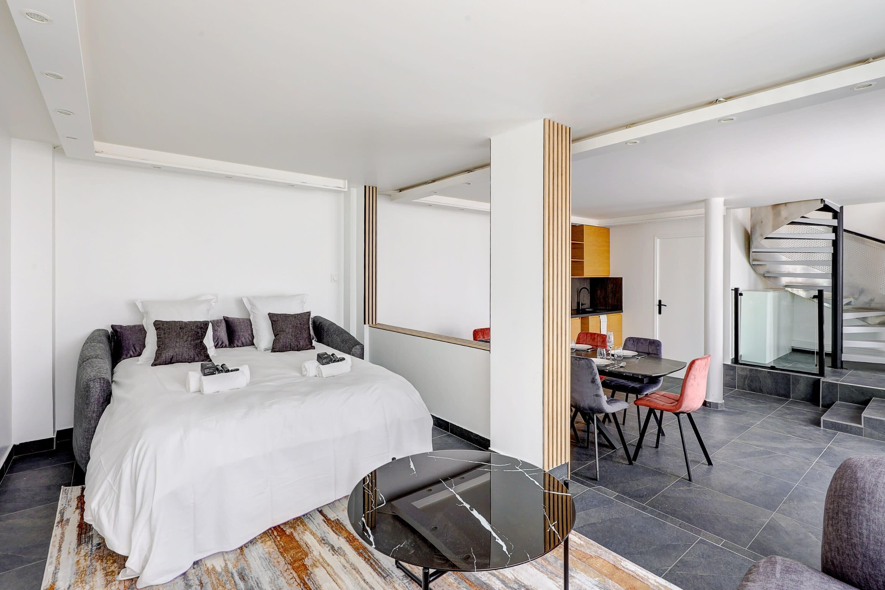 A modern hotel room with a bed, a dining area, and a spiral staircase.