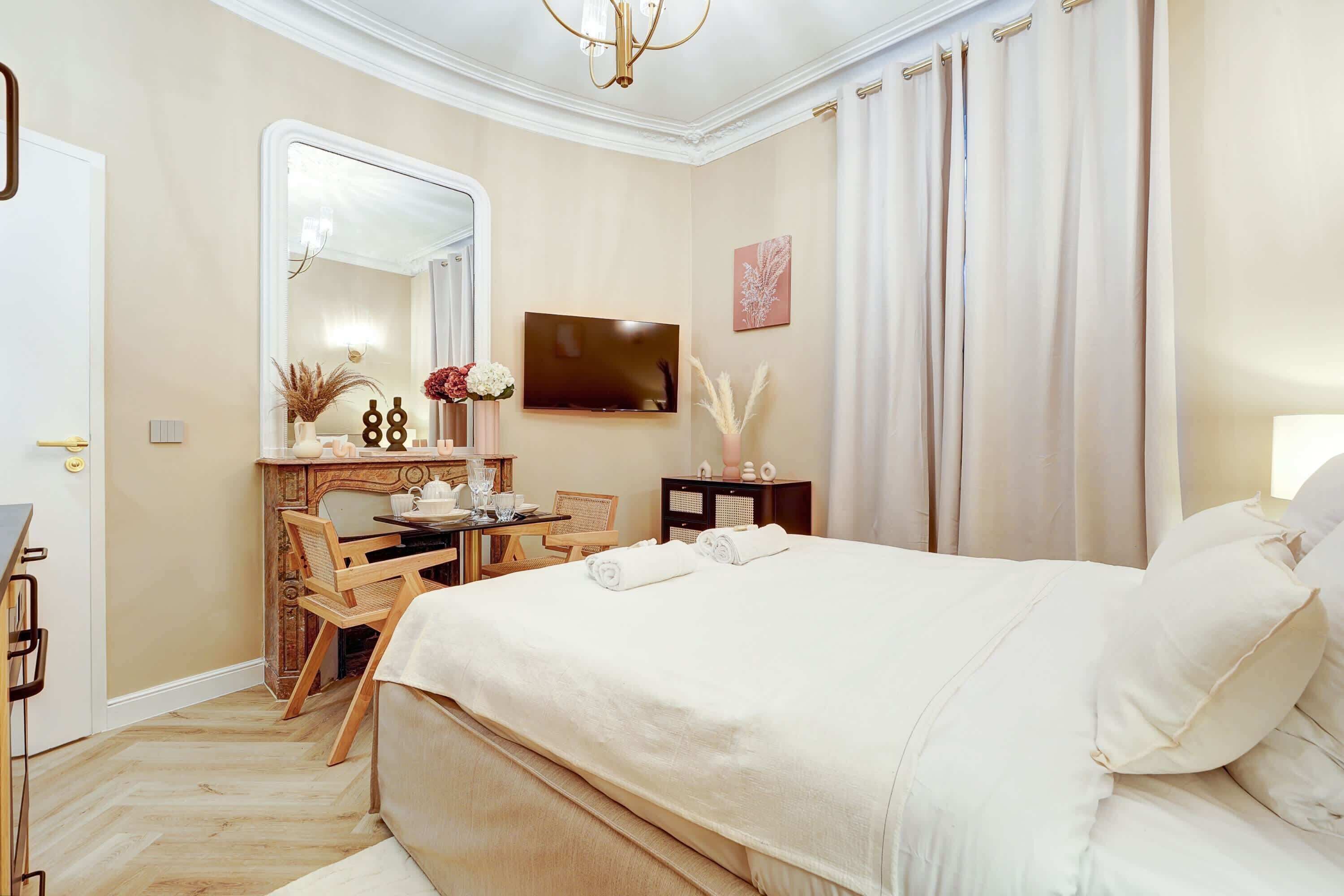 A hotel room with a large bed, a desk with a chair, a television, and a mirror.
