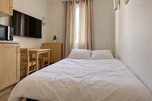 Un dormitorio con cama, escritorio, silla, televisor y una planta.