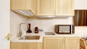 A compact kitchen with wooden cabinets, a stainless steel sink, a microwave, and a coffee maker.