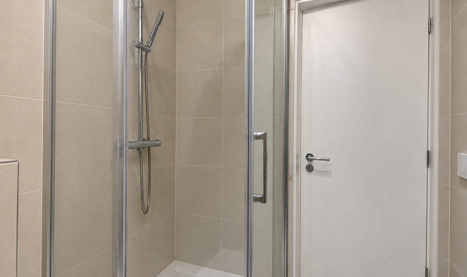 A glass-enclosed shower with a handheld showerhead and a wall-mounted faucet.