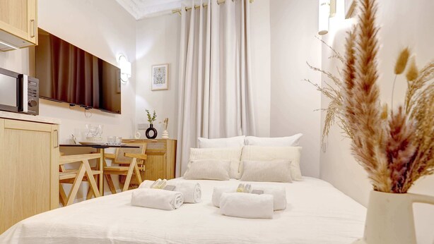 A hotel room with a bed, a desk with a chair, a microwave, and a vase with dried plants.