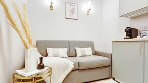 A modern living room with a grey sofa, a small side table, a white vase, and a framed artwork on the wall.