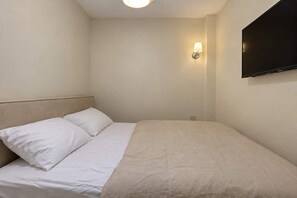 A single bed with white bedding, a headboard, and a wall-mounted TV. - Charmant cocon à Belleville • Paris • 3 personnes (Paris)