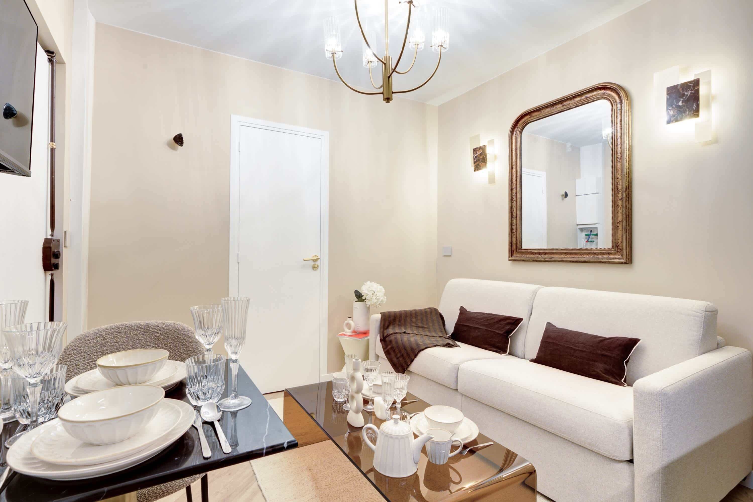 Un salon moderne avec un canapé blanc, une table basse en verre et un coin repas avec des assiettes et des verres.