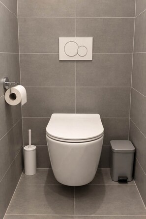 Een moderne badkamer met een toilet, een prullenbak en een toiletrolhouder.