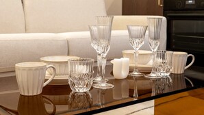 Una mesa de comedor con cubiertos de vidrio transparente y vajilla de cerámica blanca.