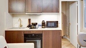 Cocina compacta con armarios de madera, horno integrado, microondas y cafetera.