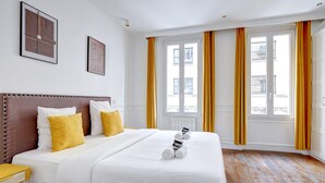 Et hotelværelse med en stor seng, trægulv og et vindue med gule gardiner.