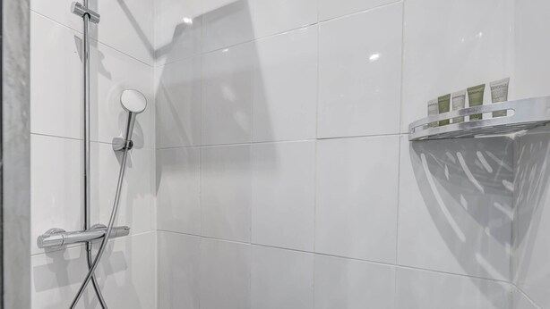 Un bagno moderno con piastrelle bianche, cabina doccia in vetro e ripiano con articoli da toilette.