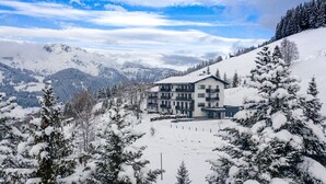 A multi-story building with balconies, surrounded by snow-covered trees and mountains in the background. - Premium Apartment With Balcony (Sankt Martin am Tennengebirge)