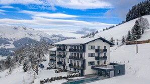 A multi-story hotel with balconies, a swimming pool, and a view of snow-covered mountains. - Premium Apartment With Balcony (Sankt Martin am Tennengebirge)