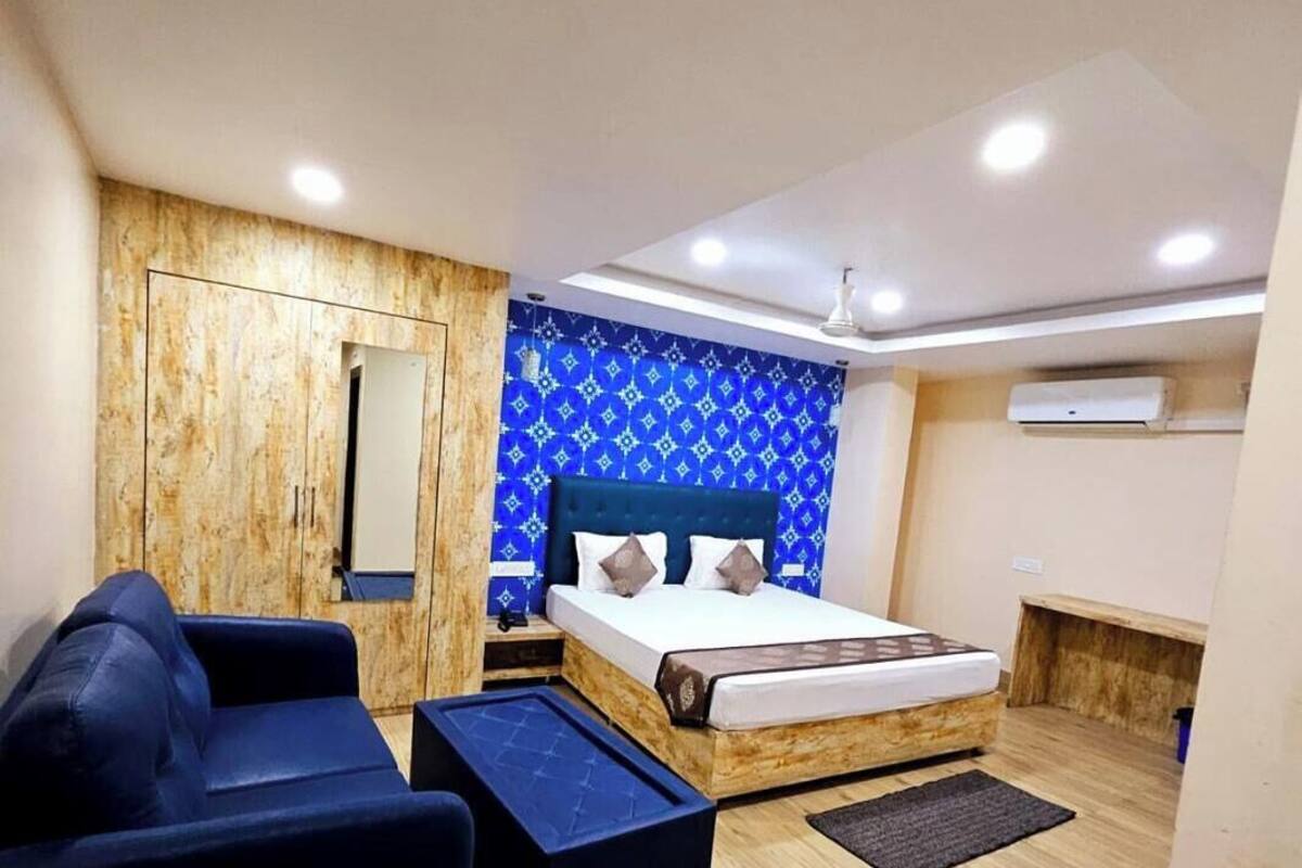 A modern bedroom with a wooden wardrobe, a bed with a blue headboard, a blue sofa, and a small table.