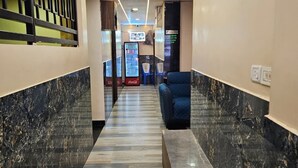 Ein Hotelkorridor mit Marmorboden, einem Coca-Cola-Kühlschrank und einer Sitzecke.
