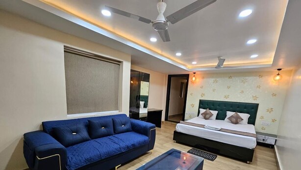 Ein modernes Hotelzimmer mit einem blauen Sofa, einem Glastisch, einem Bett mit grünem Kopfteil und einem Deckenventilator.