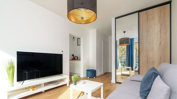 A modern living room with a flat-screen TV, a white coffee table, a grey sofa, and a wooden floor. - MARGI Lotus Apartment (Szczecin)