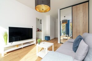 A modern living room with a flat-screen TV, a white coffee table, a grey sofa, and a wooden floor. - MARGI Lotus Apartment (Szczecin)