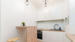A modern kitchen with white cabinets, a wooden countertop, a built-in oven, and a sink. There is a stool and a small plant on the countertop. - MARGI Lotus Apartment (Szczecin)