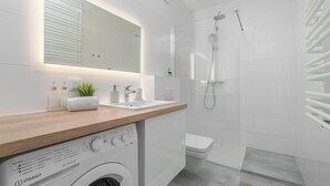 A modern bathroom with a washing machine, a sink, a toilet, and a shower. - MARGI Lotus Apartment (Szczecin)