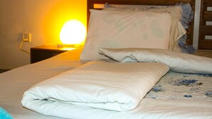 Una cama bien hecha con edredón blanco y almohadas, cabecera de madera y lámpara de noche con luz amarilla.