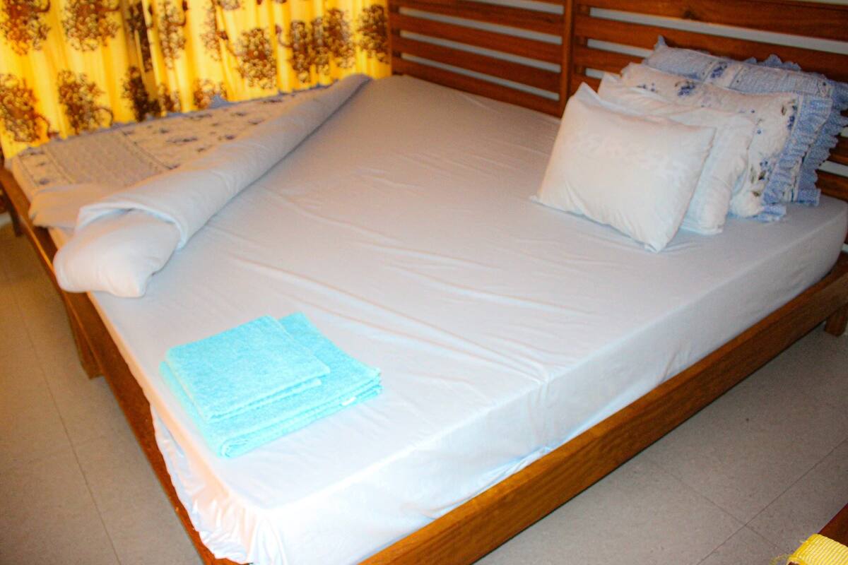 Una cama bien hecha con sábanas blancas, una toalla enrollada y una pila de toallas dobladas.