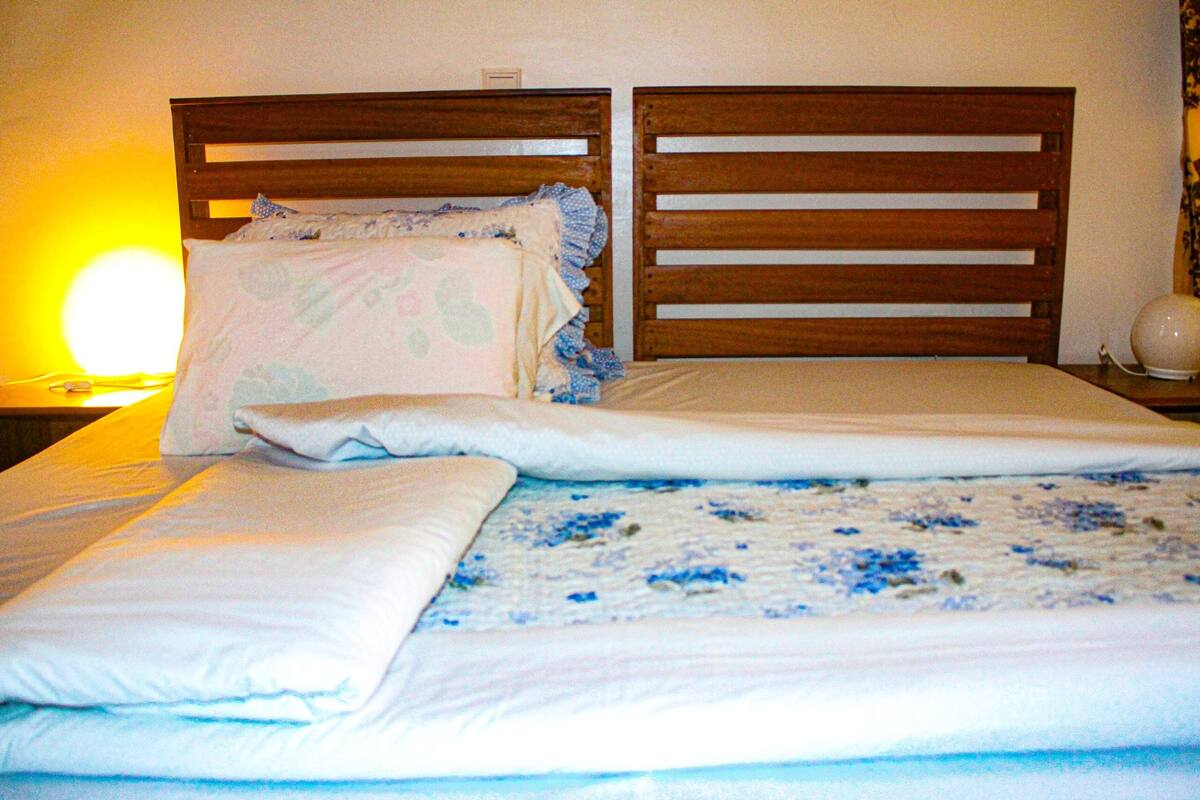 Una cama con cabecera de madera, almohada blanca y manta azul con estampado floral.