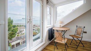 Une pièce dotée de grandes fenêtres, d’une table avec des chaises, et offrant une vue sur une étendue d’eau et des bâtiments.