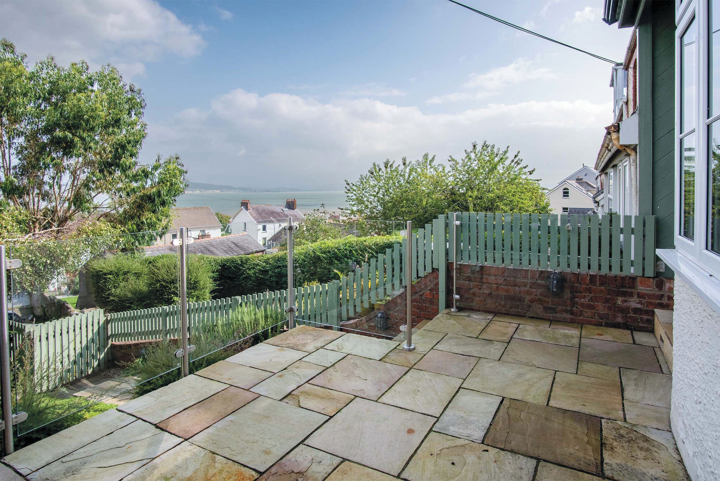 Eine Terrasse mit Steinboden, einem weißen Zaun und Blick auf das Meer.