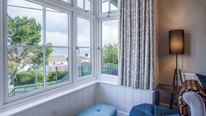 Une pièce dotée d’une grande baie vitrée, d’un banc bleu, d’une lampe et offrant une vue sur la mer et la verdure.