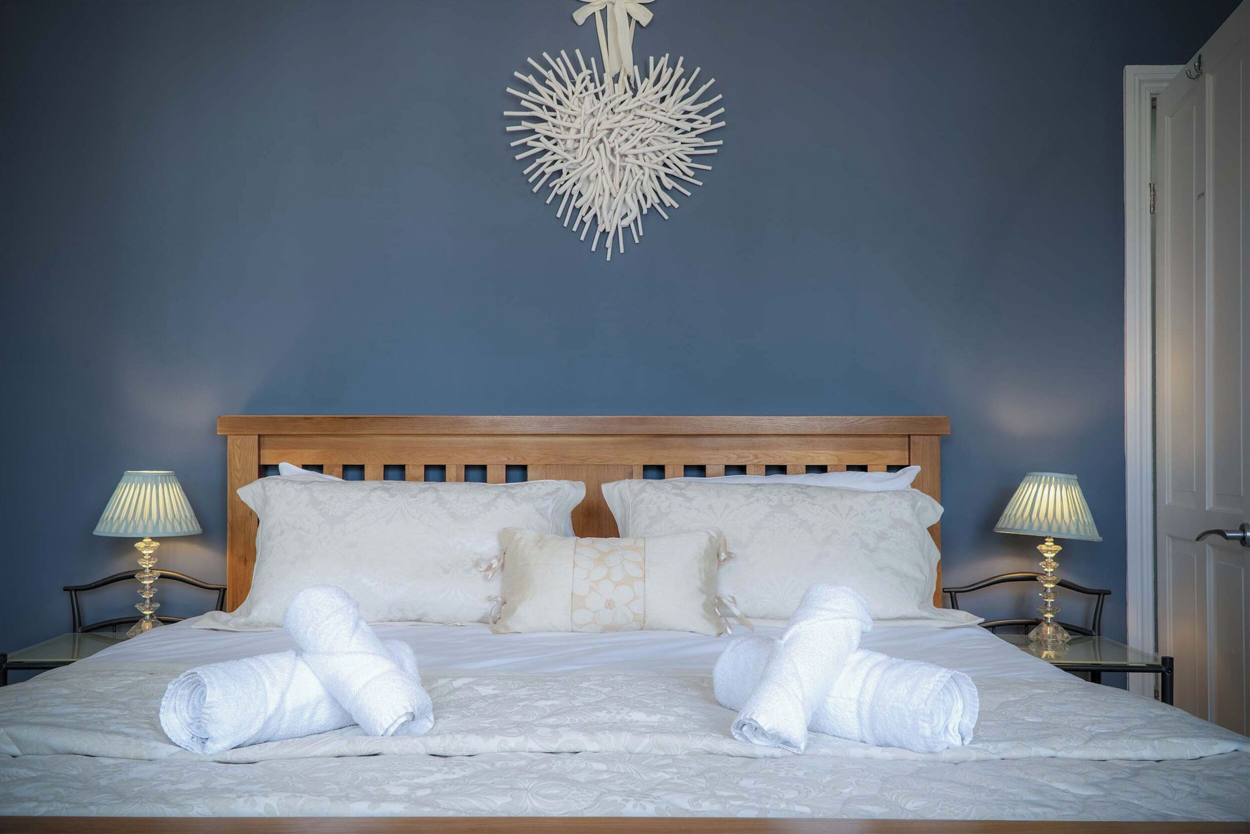 A neatly made bed with white linens and towels, two bedside lamps, and a decorative hanging light fixture.