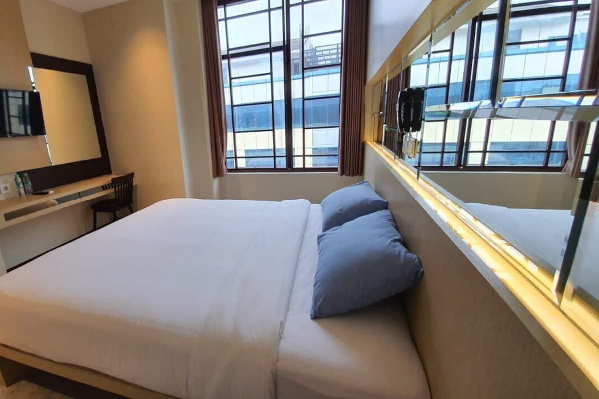 A hotel room with a bed, a desk, a chair, a TV, and a window with a view of the city.