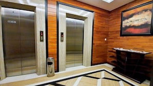 An elevator area with two elevators, a trash bin, and a wall-mounted display unit. - MP Hotel Kelapa Gading (Jakarta)